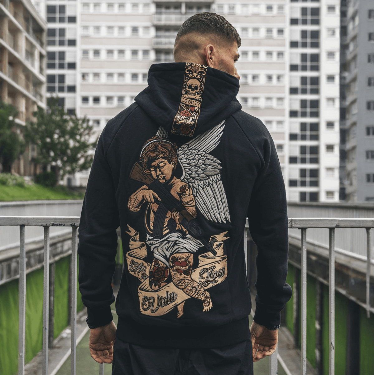 Achterkant van de Cupid with gun hoodie met geborduurde engel met geweer, gedragen buiten bij flats
