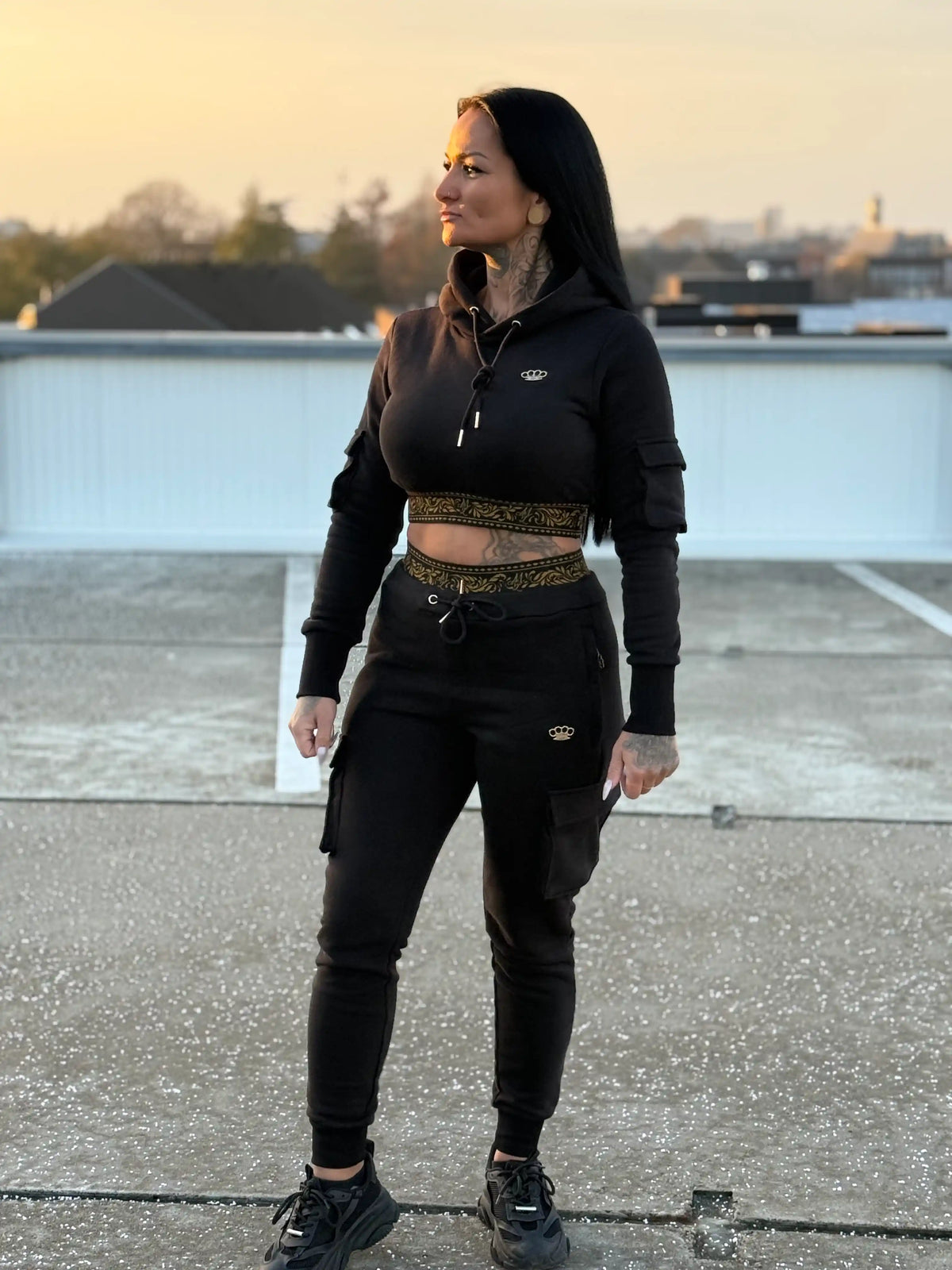 Model in de MVL Meander dames hoodie en joggingbroek op een dak bij zonsondergang