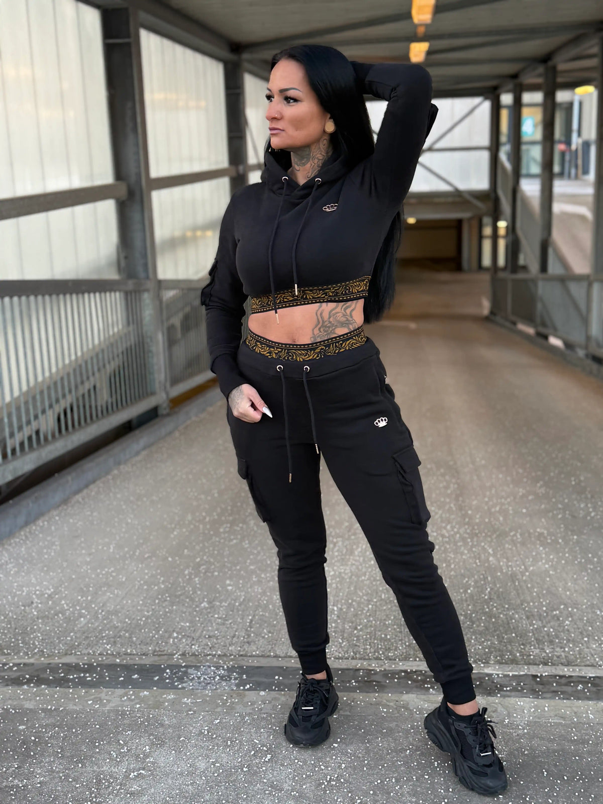 Model in het zwarte MVL Meander dames trainingspak met cropped hoodie op een loopbrug