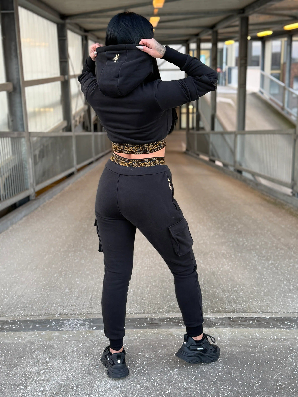 Model toont de achterkant van het MVL Meander dames trainingspak met de handen aan de capuchon