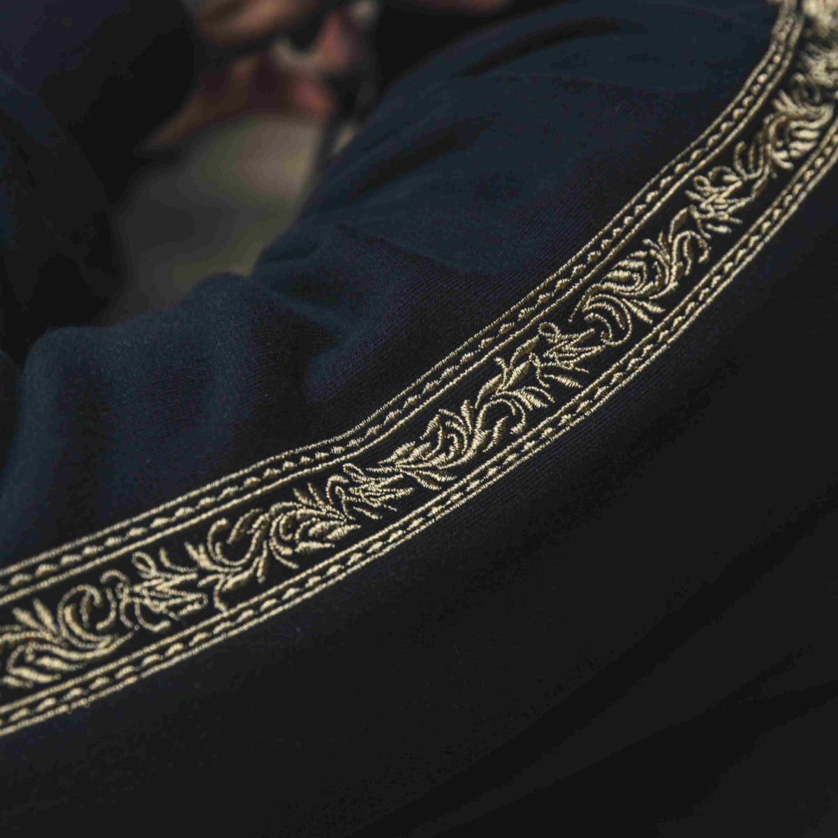 Close-up van de gouden embroidery band op de mouw van het MVL Meander trainingspak