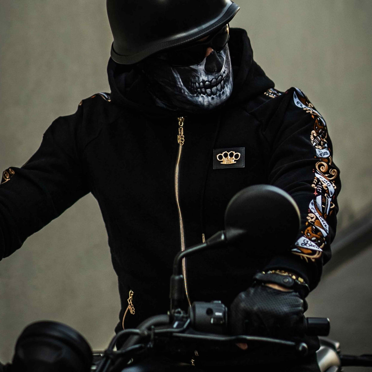 Model w masce czaszki i kasku w czarnej bluzie Savage ornate na motocyklu