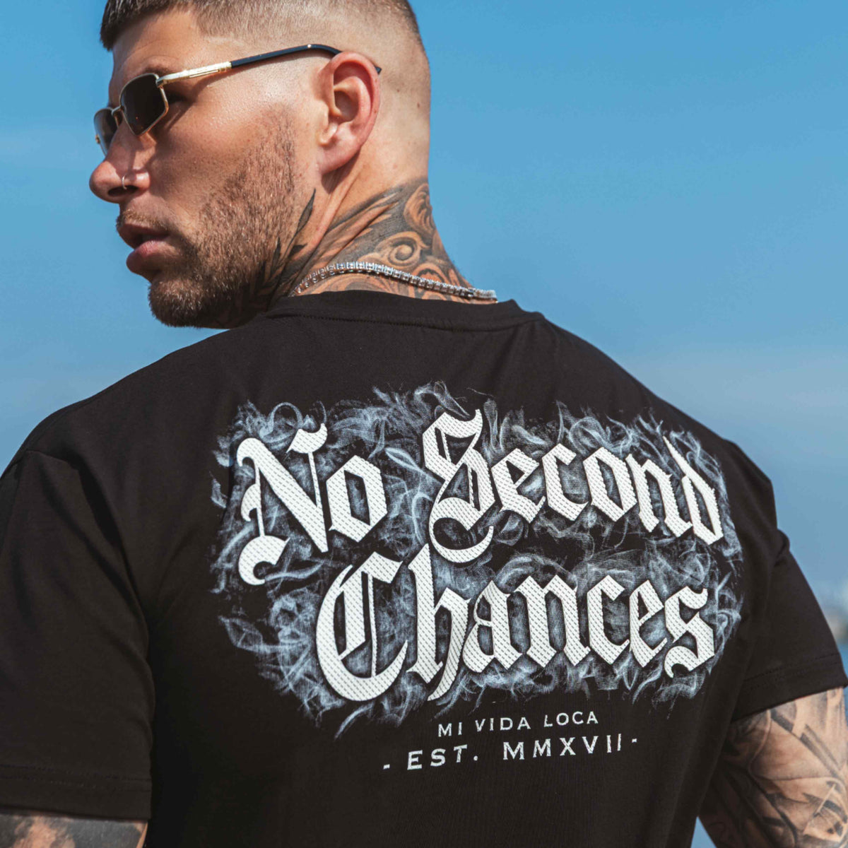 Model w okularach przeciwsłonecznych w czarnej koszulce No second chances, nadruk na plecach widziany przez ramię