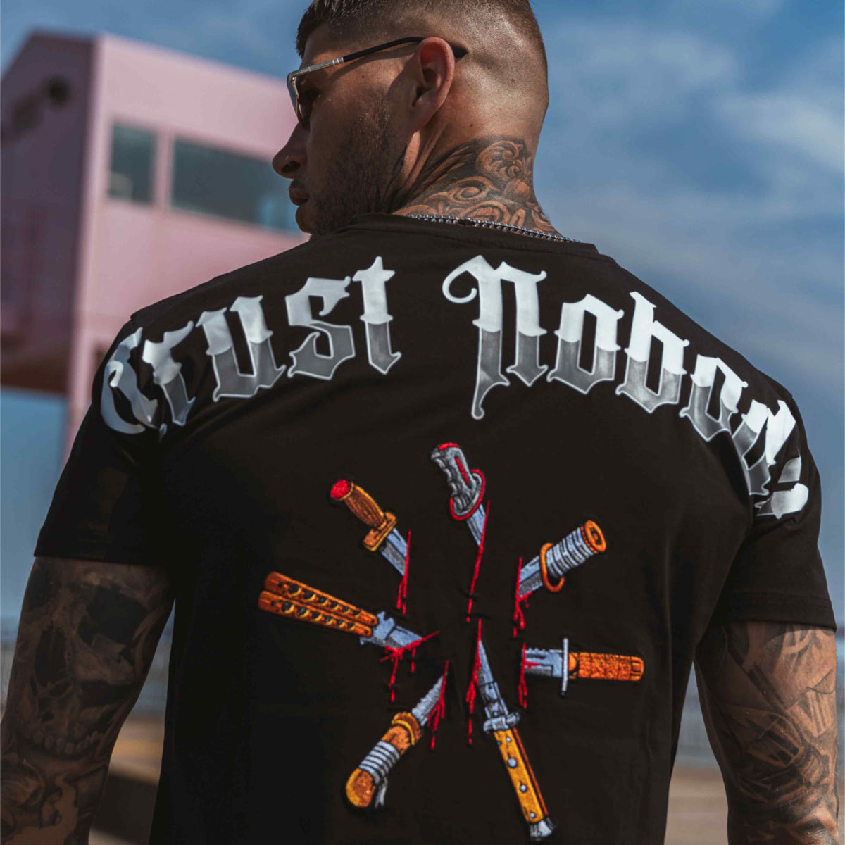 Model met zonnebril in het zwarte Trust nobody back stab T-shirt, van achteren gezien