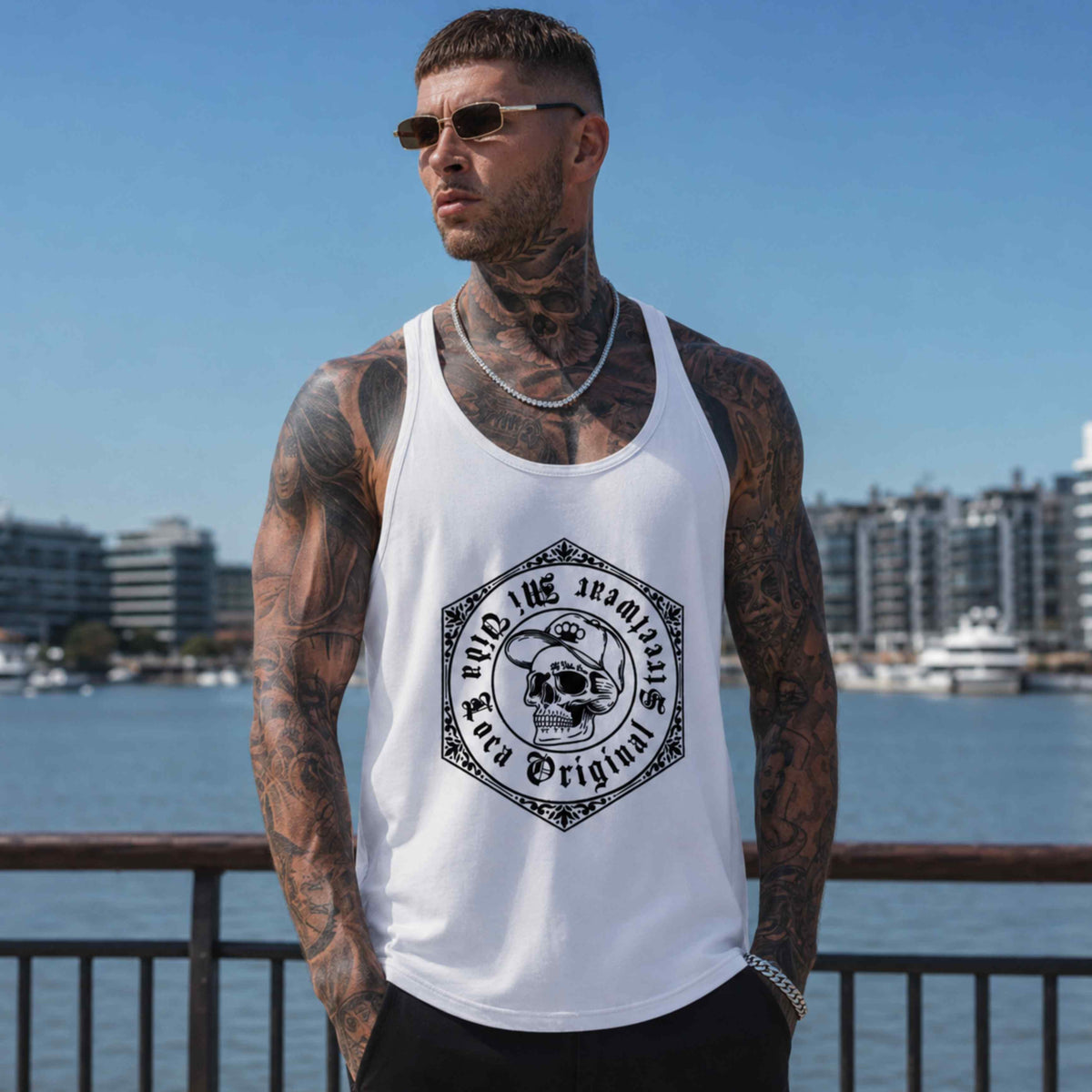 Model in witte MVL Original streetwear tanktop met skull-print bij reling, haven op achtergrond