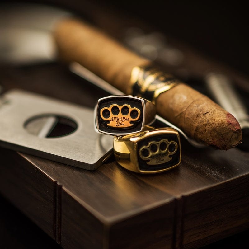 Anelli con sigillo MVL argento e oro accanto a un sigaro e un tagliasigari su legno