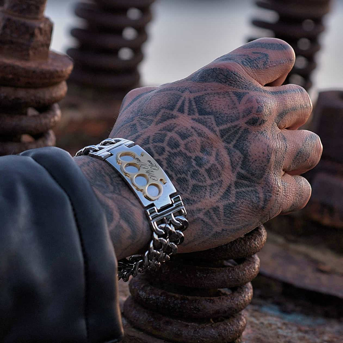 MVL bracelet in silver/gold on a tattooed hand on rusty metal coils