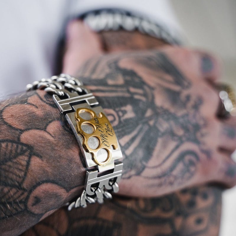 Silver MVL bracelet with gold MVL logo on a tattooed wrist, close-up